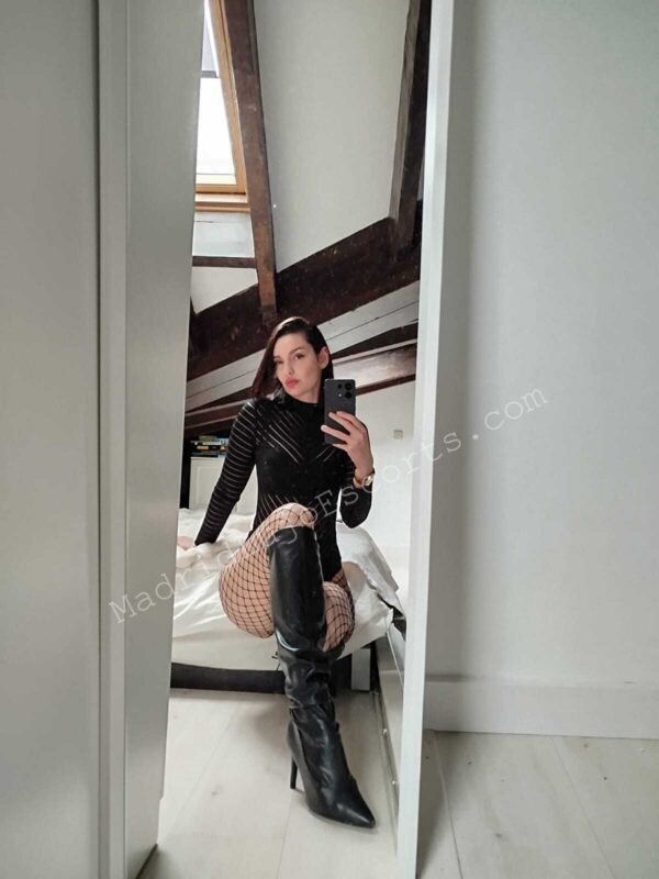 Angelina con un vestido corto negro y botas de cuero en Madrid haciéndose una foto con una mirada sensual