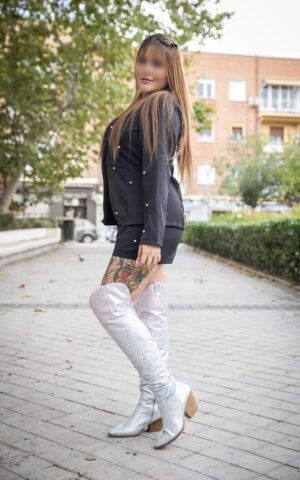Dulce, escort colombiana de lujo en Madrid posando al aire libre con botas plateadas y vestido negro