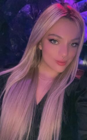 Melody escort argentina de lujo en Madrid con cabello rubio y fondo oscuro, selfie casual