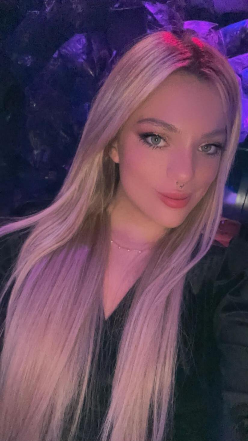 Melody escort argentina de lujo en Madrid con cabello rubio y fondo oscuro, selfie casual