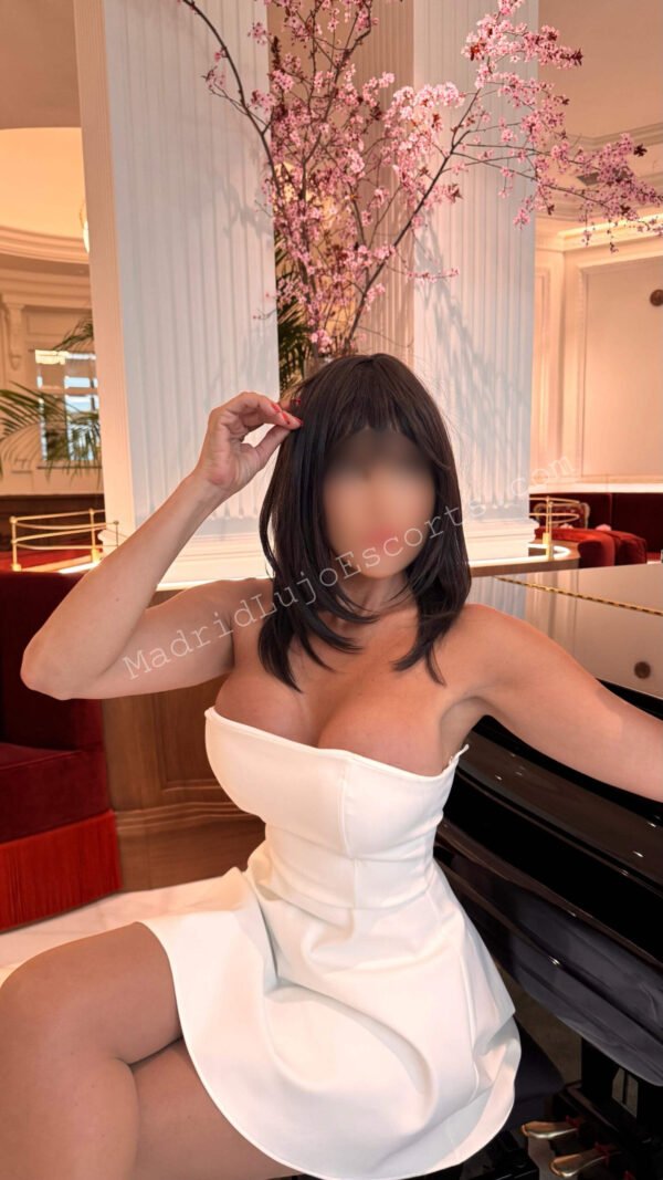 Vanessa sentada junto a un piano con outfit blanco en ambiente lujoso