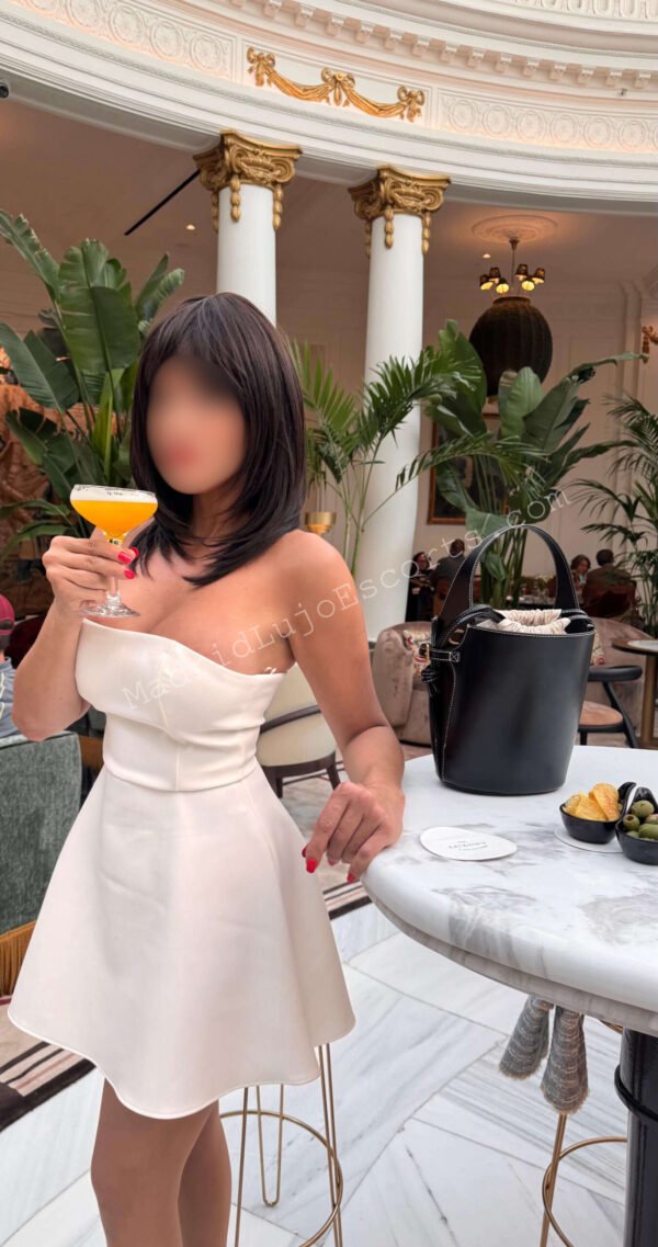 Vanessa con vestido blanco y copa en la mano en un entorno cálido y chic