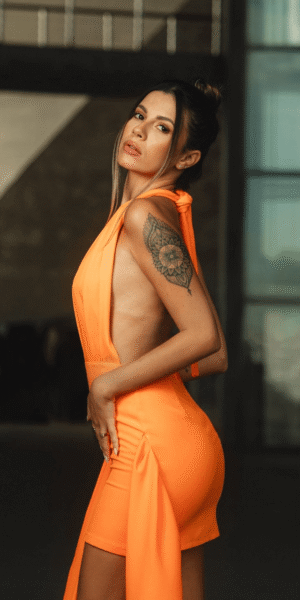 Agatha escort brasileña de lujo en Madrid en vestido naranja ajustado, perfil sensual