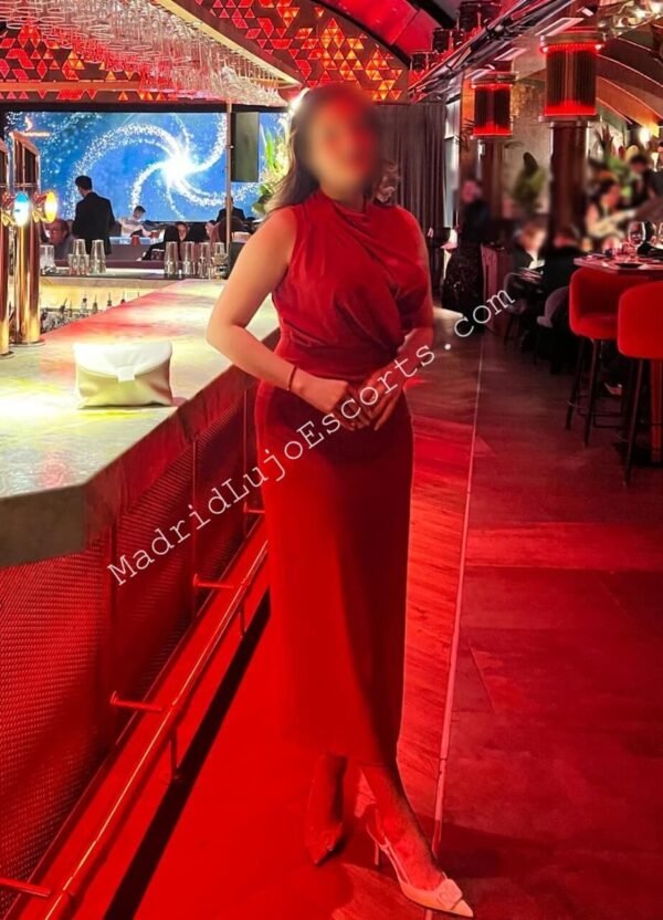 Belén, escort española de lujo con vestido rojo en un bar elegante con luces