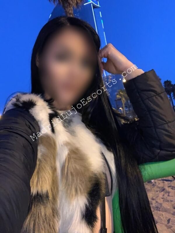 Elektra, escort brasileña de lujo con abrigo y bufanda de piel posando de noche