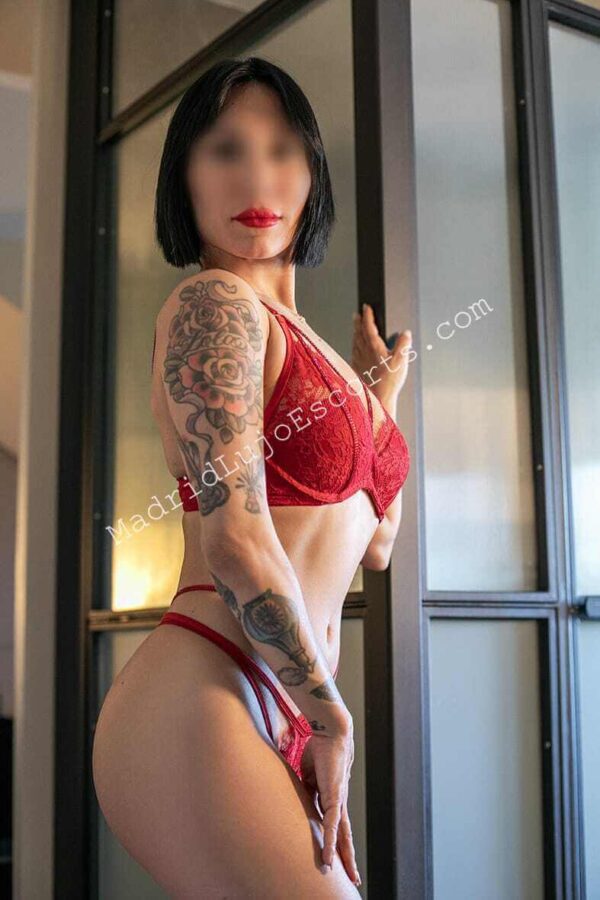 Emma escort española en Madrid en lencería roja posando junto a ventana