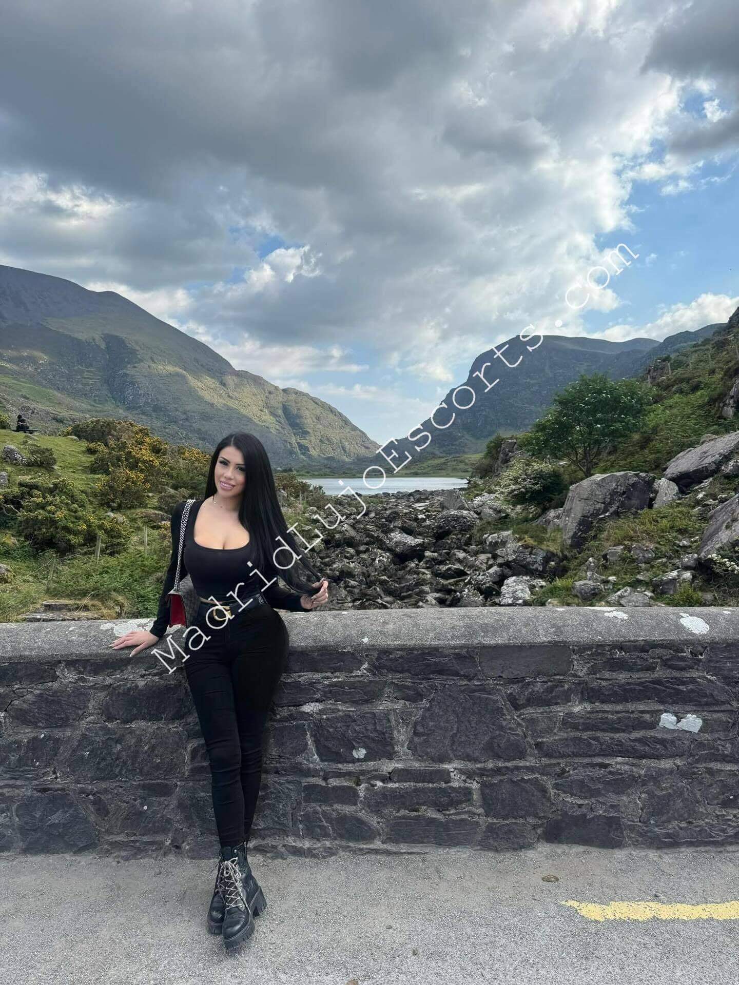 Brendi escort chilena en Madrid posando en un paisaje natural con ropa oscura