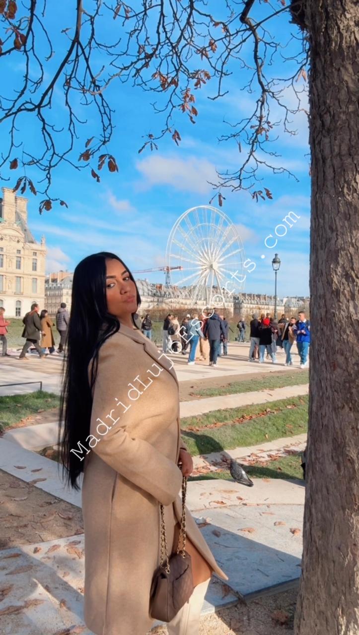 Aline, escort Madrid posando en exterior con abrigo claro