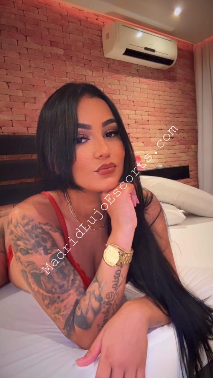 Aline, escort Madrid posando en interior con lencería roja sobre una cama