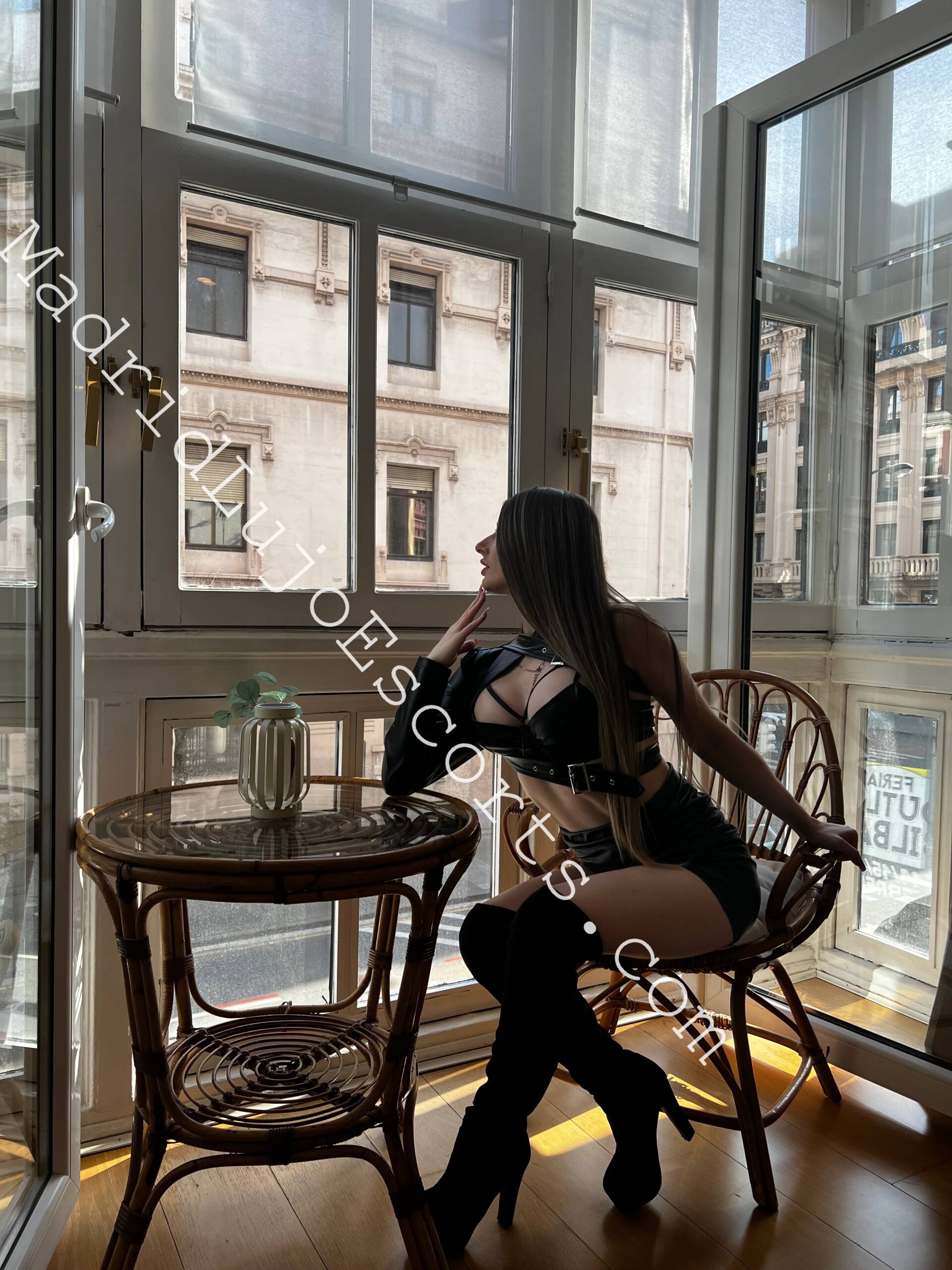 Larissa escort rusa en Zaragoza sentada junto a un ventanal con un look elegante