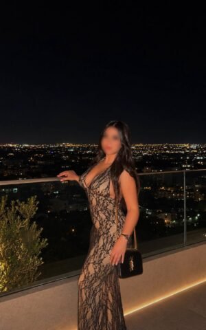 Anghie, escort en Madrid posando con vestido largo en una terraza con vistas nocturnas