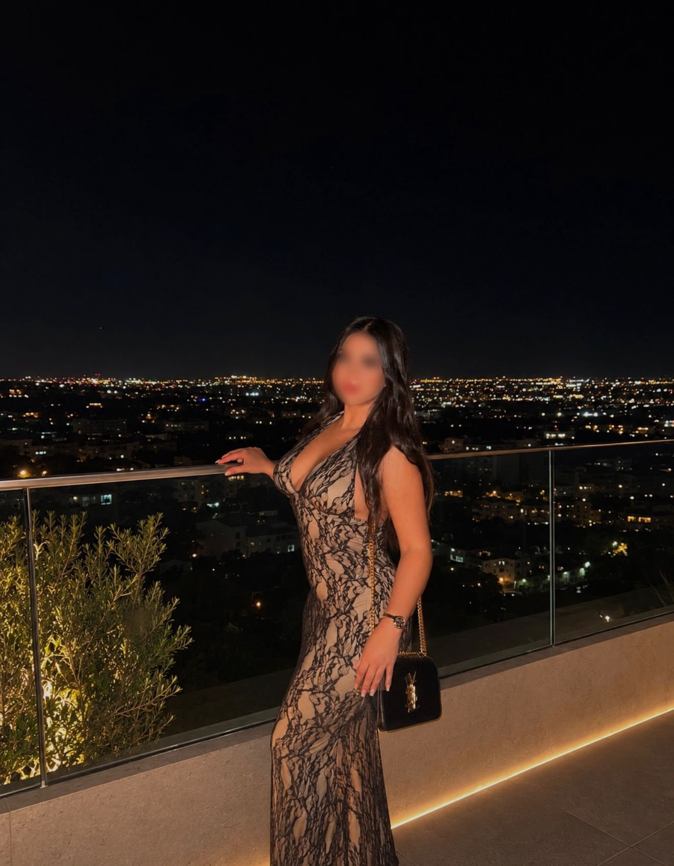 Anghie, escort en Madrid posando con vestido largo en una terraza con vistas nocturnas